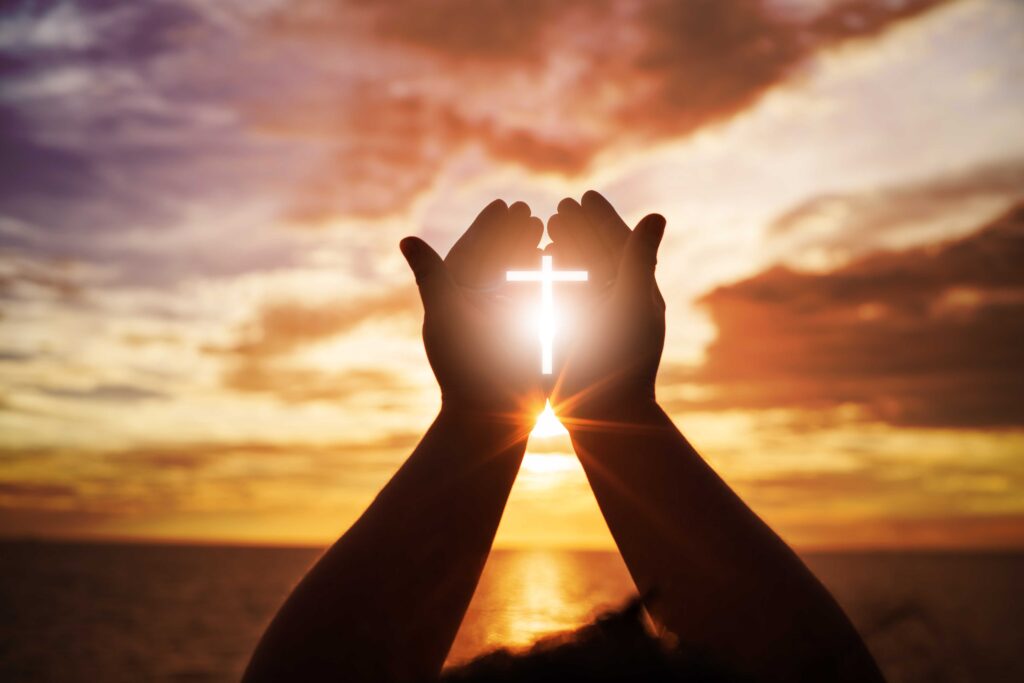 Hands lifted toward a glowing cross at sunrise
